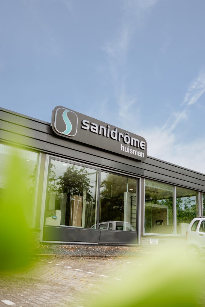 Vooraanzicht van de Sanidrõme Huisman showroom in Gouda met grote ramen en het logo op de gevel